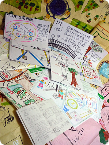 写真：お送り頂いた作品の数々。模造紙や画用紙等にかかれた色とりどりの絵や、工夫のポイントを説明する文章