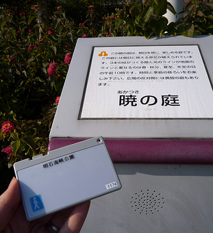 写真：案内板と音声案内用の無線カード。カードの大きさは、縦5センチ横9センチくらいで薄い。角の側面にスライドさせる小さなボタンが付いている