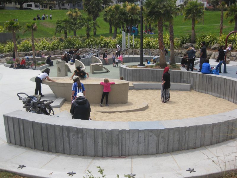 写真：扇形をした砂場の要の位置には、車いすでアクセスできるよう腰高くらいのレイズド砂場。船型のそれを囲むように子どもたちが立って遊んでいる