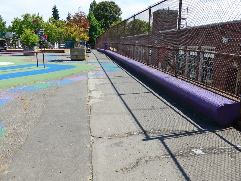 写真：校舎との境のフェンス沿いにある長いベンチの前をくねくねと延びる道