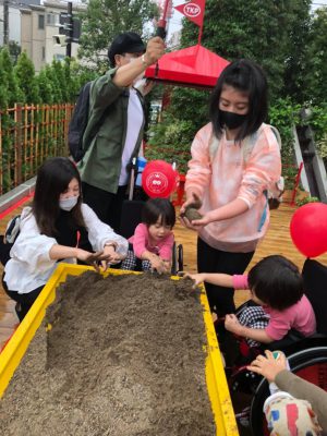 写真:サンドテーブルで遊ぶ鈴木さん一家。車いすから砂に手を伸ばす双子の男の子