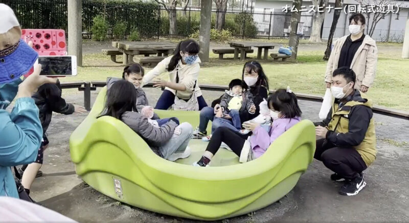 写真：回転遊具を楽しむメンバーたち。子どもを前に抱いてシートに座る親も笑顔