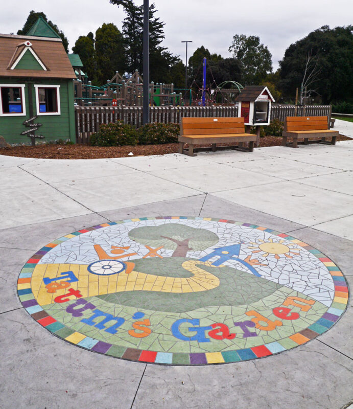 写真：エントランス広場の地面に円形のモザイク画。カラフルなタイルで表現されているのは、車いすユーザーを含む子どもたちが楽しむ様子と遊び場のロゴ