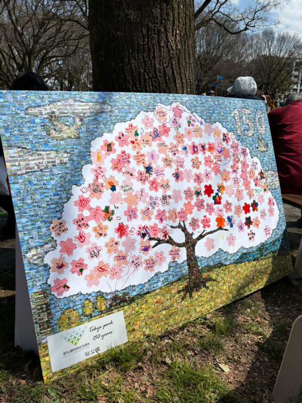写真：大きな木のシルエットが描かれたパネル。来訪者が桜の形をした付箋に絵やコメントを自由に書いて貼ることができる。