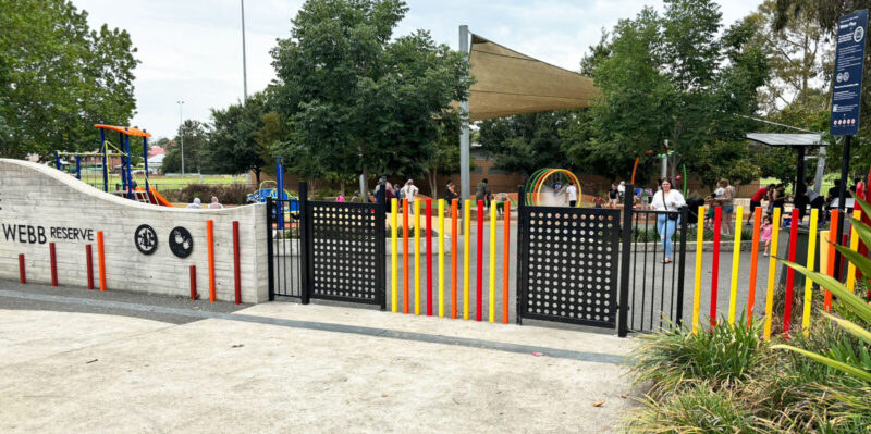 写真：石塀と細い柱の柵が連なる中、出入口として格子状の片開き扉が2カ所。