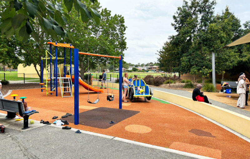 写真：幼児用エリア。ゴムチップ舗装のスペースに小さなブランコや滑り台、スプリング遊具などが並ぶ。