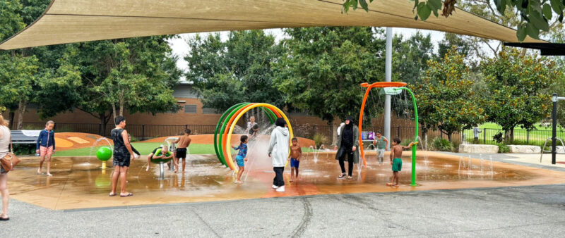 写真：水遊び場で遊ぶ異年齢の子どもたち。ヒジャブをまとった母親は自分も水浸し状態。