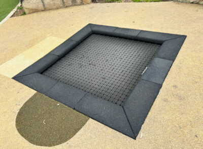 写真：トランポリンの縁には、衝撃を吸収するゴムチップ舗装の黒いタイル。その周りに広がるエリア全体の地面は、クリーム色のゴムチップ舗装。