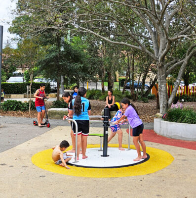 写真：アクセシブルな回転遊具。回転盤は地面とフラットで、手すりとベンチ付き。5人の子どもが裸足で遊んでいる。