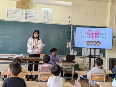 写真:教室で子どもたちに話すメンバー二人。