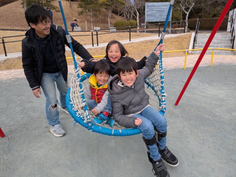 写真:友達と3人で皿型ブランコに乗り笑顔の男の子。