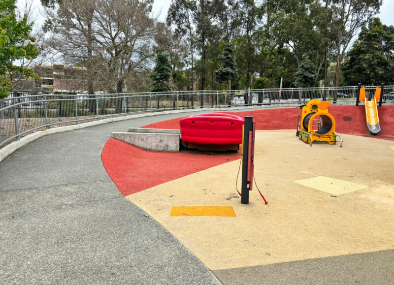 写真：土手の上り口。スロープの左側に柵。土手の斜面は赤で、広場の地面は黄色。