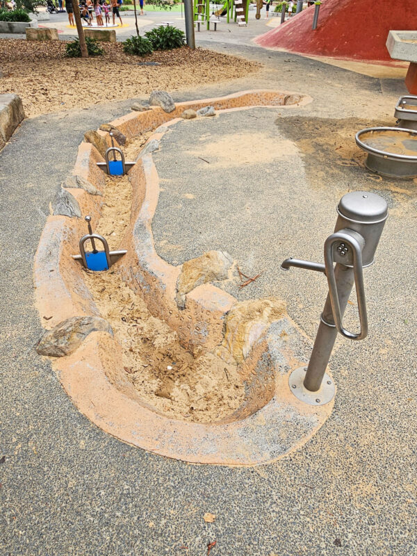 写真：手押しポンプの下から延びる長さ10メートル弱の水路。所々に岩が配され可動式の堰が2つある。