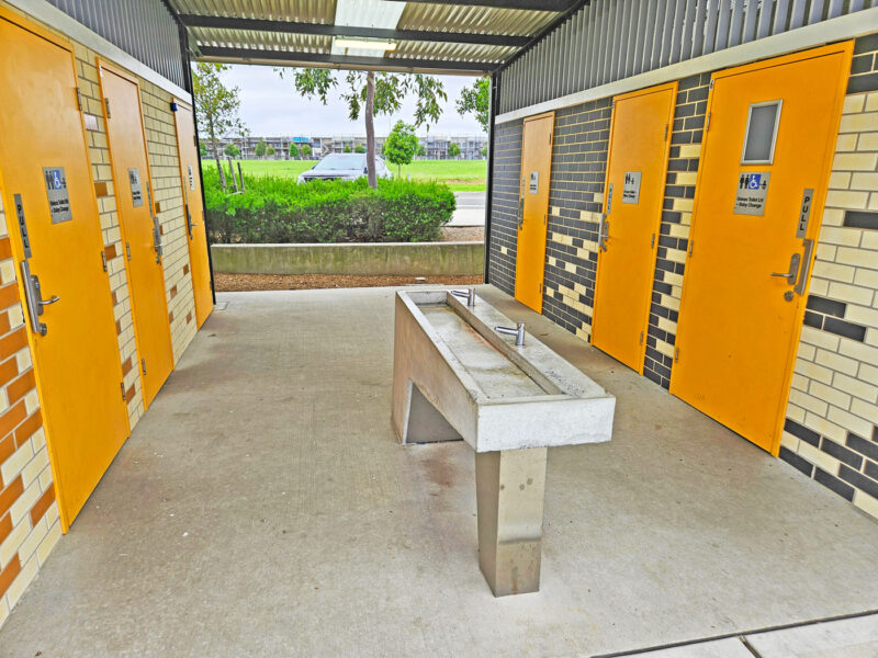 写真：中央に手洗い場。両側に3つずつ並んだトイレの個室。